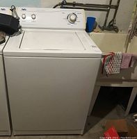 Front view of white Inglis top-loading washing machine in basement area with sink and towels nearby.