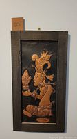 Framed copper relief artwork of an indigenous figure in profile, holding a flame-like object, with detailed traditional attire and headdress, framed in dark wood.