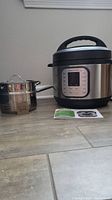 Aroma Instant Pot Duo Nova alongside Ecko steamer pot and lid on floor with instruction manuals.