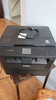 Brother HL-L2390DW laser printer with visible USB cable on top and some wear marks on surface.