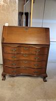 Front view of closed mahogany secretary desk showing curved dovetail drawers and claw feet