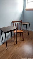 Photo of two dark wood side tables and one wooden chair in a room with hardwood floor.