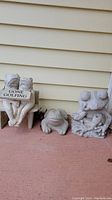 Photo of three frog-themed cement garden pieces: a frog holding 'Gone Golfing' sign on a bench, a small frog figurine, and two frogs on a box.