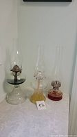Photo showing three vintage glass oil lanterns in green, yellow, and red with clear chimneys