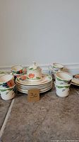 Photo showing cups, plates, and covered sugar bowl with floral design and gold trim on tile floor.