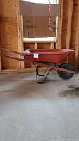 Side view of wheelbarrow showing rust-colored plastic tub, metal handles, and single rubber wheel.