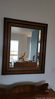 Straight-on photo of the wood framed mirror mounted on a wall, showing reflective surface and wooden frame detail.