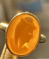 Close-up of oval shell cameo showing white female profile on orange background.