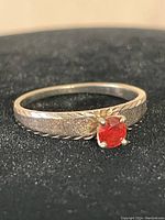 Front view of ring on black background showing band texture and solitaire red stone