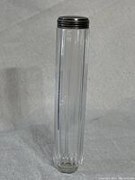 Full view of the tall, cylindrical clear glass toothpaste powder jar with vertical ribbing and octagonal base.