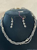 Full view of the hematite and seed pearl torasade necklace with matching earrings on a black display bust, showing intricate beadwork and gold ball accents.