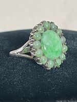 Front angle showing large polished oval jade and surrounding smaller jade stones in ornate silver setting on split band.