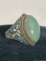 Close-up side view showing the green jade stone and detailed blue enamel floral designs on the silver band.