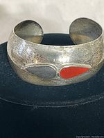 Front view of sterling silver cuff bracelet showing gray and orange-red teardrop stone inlays on textured surface.