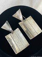 Front view of the pair of sterling silver earrings showing the rectangular and triangular design with mixed textured and polished finishes.