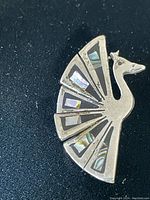 Close-up photo of the sterling silver peacock brooch laid on a black surface, showing abalone inlay details and shape.