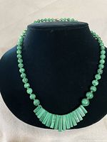 Full view of the necklace displayed on a black bust, showing the green malachite beads with a fan style pendant.
