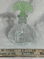 Front angle view of clear glass perfume bottle with jadeite fan-shaped stopper showing curved embossed swirl design on bottle front.