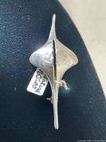 Top view showing polished elongated diamond-shaped brooch with wavy center split and attached 925 stamped tag.