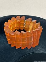Full front view of wide amber translucent resin cuff bracelet displayed on black stand.