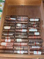 Wooden box filled with 31 plastic coin tubes containing rolled pennie coins, each tube labeled with date ranges of the coins inside.