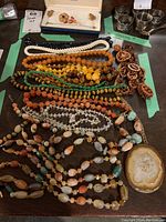 Overview of multiple necklaces laid out on a table showing various bead colors and textures, including tiger's eye and agate with pendant, wooden beads, and clear glass beads.