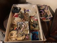 Box full of assorted costume jewelry including pearl necklaces, bead bracelets, earrings, and chains.