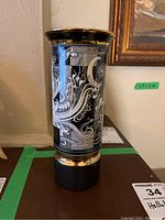 Front view of cylindrical vase showing intricate white swirl motif on black background with gold rim