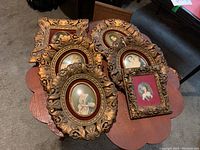Top view of six gold-colored ornate frames with miniature prints of women in period attire, laid out on a scalloped wooden table.