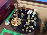 Wide top-down view of all metal and ceramic miniatures arranged on black circular surfaces showing various figurines, salt cellars, vases, and stands.