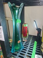 Photo showing two glass vases on a shelf: a tall green and clear Murano style vase labeled 15, and a smaller red and yellow faceted vase labeled 8.