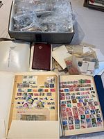 Overview of box with plastic bags of stamps, pile of glassine envelopes, loose stamps and binder on tabletop