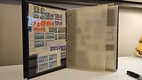 Front inside view of black stamp album showing multiple vintage Canadian stamps and blocks mounted on pages.