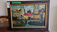Frontal view of framed oil painting showing Moulin Rouge with urban cityscape and figures. Frame shows signs of wear including scuffs.