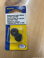 Photo of two black replacement cutter wheels packaged in clear plastic, attached to blue and yellow BrassCraft branded cardboard backing. Text on packaging indicates compatibility with T001 and T006 models and includes a lifetime warranty.