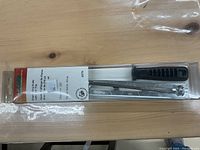 Photo of a new universal chain filing guide in original plastic blister packaging, showing the metal guide tool and a black handle tool inside, with packaging label visible.