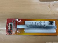 Chainsaw filing guide tool in original sealed retail packaging on cardboard backing with plastic cover. Instruction sheet visible behind tool.