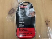 Photo shows the front of the original unopened packaging of the Craftsman Emergency Key Release. The package is black, red and silver with text in English and French. Package mounted on a wooden surface.