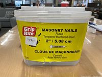 Plastic container of Grip Rite masonry nails with yellow label showing specification of 2 inch fluted tempered hardened steel nails.