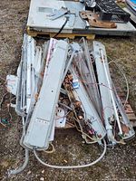 Pile of nine fluorescent light fixtures with exposed wiring and sockets.