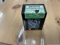 Box of round machine screws labeled 6-32 x 1 1/2 zinc plated containing multiple screws inside, placed on wooden surface.