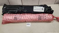 Two wrapped rolls of polyethylene vapor barrier film, one in black wrapper, one in pink, on tiled floor.