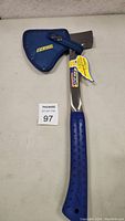 Estwing hatchet full view with blue protective sheath and attached manufacturer's tag.