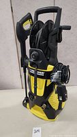 Front and side views showing Karcher logo, hose reel loaded with pressure hose, spray gun mounted to side, and attached power cord wound around hooks.
