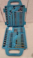 Open blue plastic case displaying all 99 pieces of the drill bit set with various bits and extensions organized in molded slots.