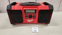 Front view showing red Milwaukee clock radio with dual black speakers, digital display and control buttons