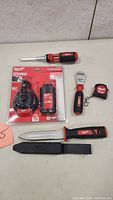Full layout of all Milwaukee tools in lot: multi-bit screwdriver, chalk reel in packaging with refill, utility knife with sheath, bottle opener, measuring tape