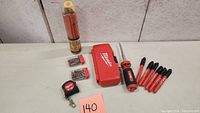Full lot overview displaying Milwaukee screwdriver, bit case, six markers, measuring tape, and pencil on table