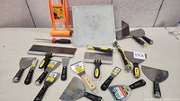 Full display of all assorted putty knives, taping knives, and trowels laid out on table.