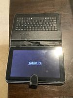 Tablet powered on showing 'Tablet PC Keep Moving Forward' splash screen, placed in black case with integrated keyboard.